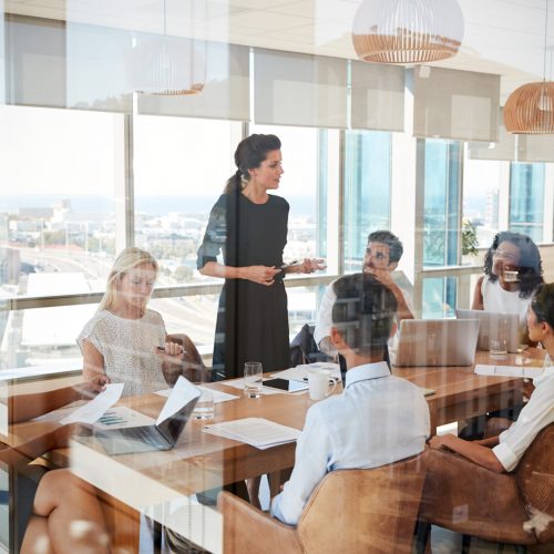 Businesswoman Leads Meeting Around Table Shot Through Door